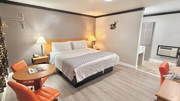 Una habitación de hotel con una cama, dos lámparas de noche, una mesa redonda de madera, una silla naranja y un pequeño escritorio con una silla.