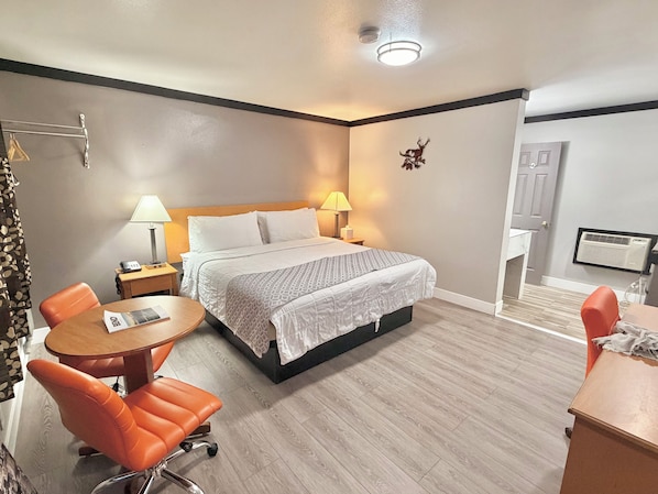Une chambre d’hôtel avec un lit, deux lampes de chevet, une table ronde en bois, une chaise orange et un petit bureau avec une chaise.