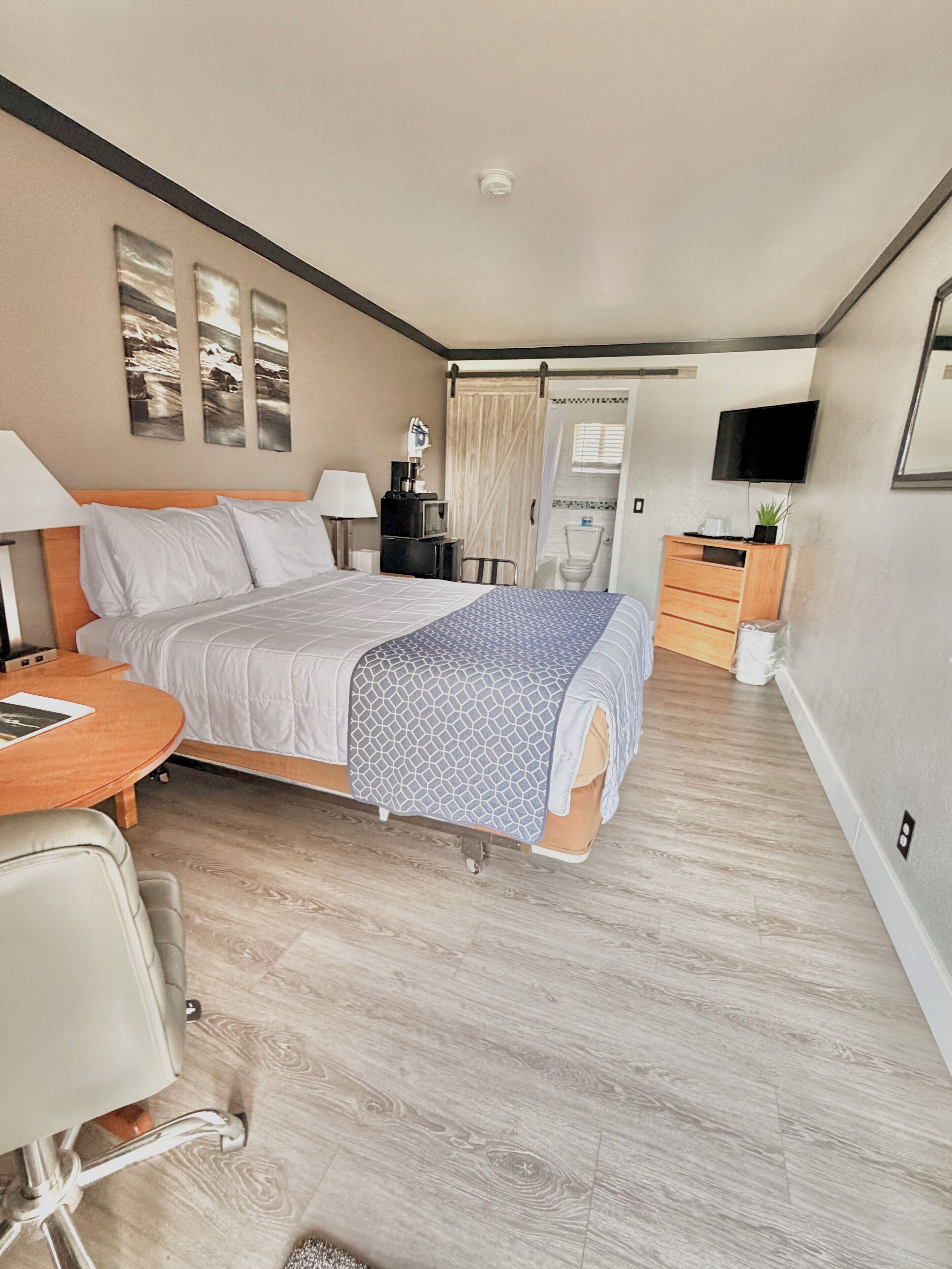 Habitación de hotel con cama, mesita de noche, lámpara, silla y una pequeña mesa.