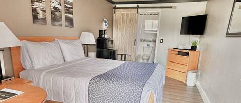 A hotel room with a bed, bedside table, lamp, chair, and a small table.