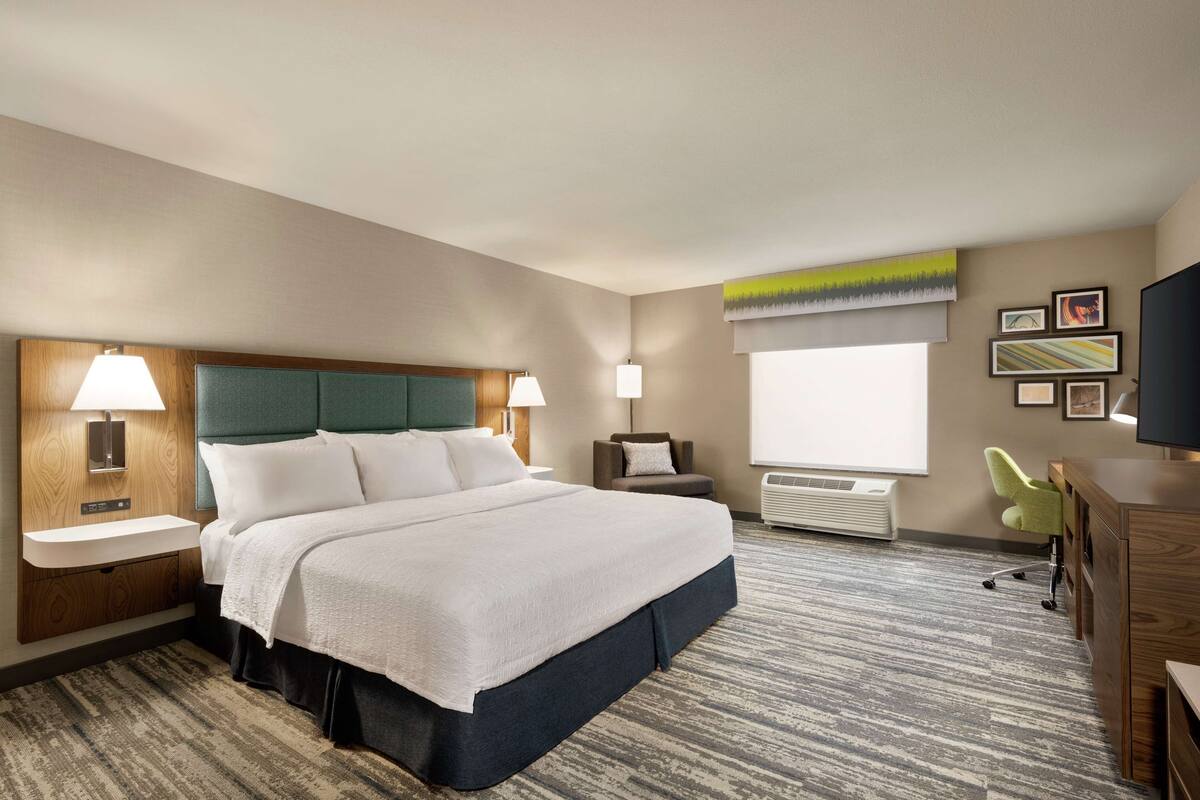 A hotel room with a large bed, a desk, a chair, a TV, and a window with a view.