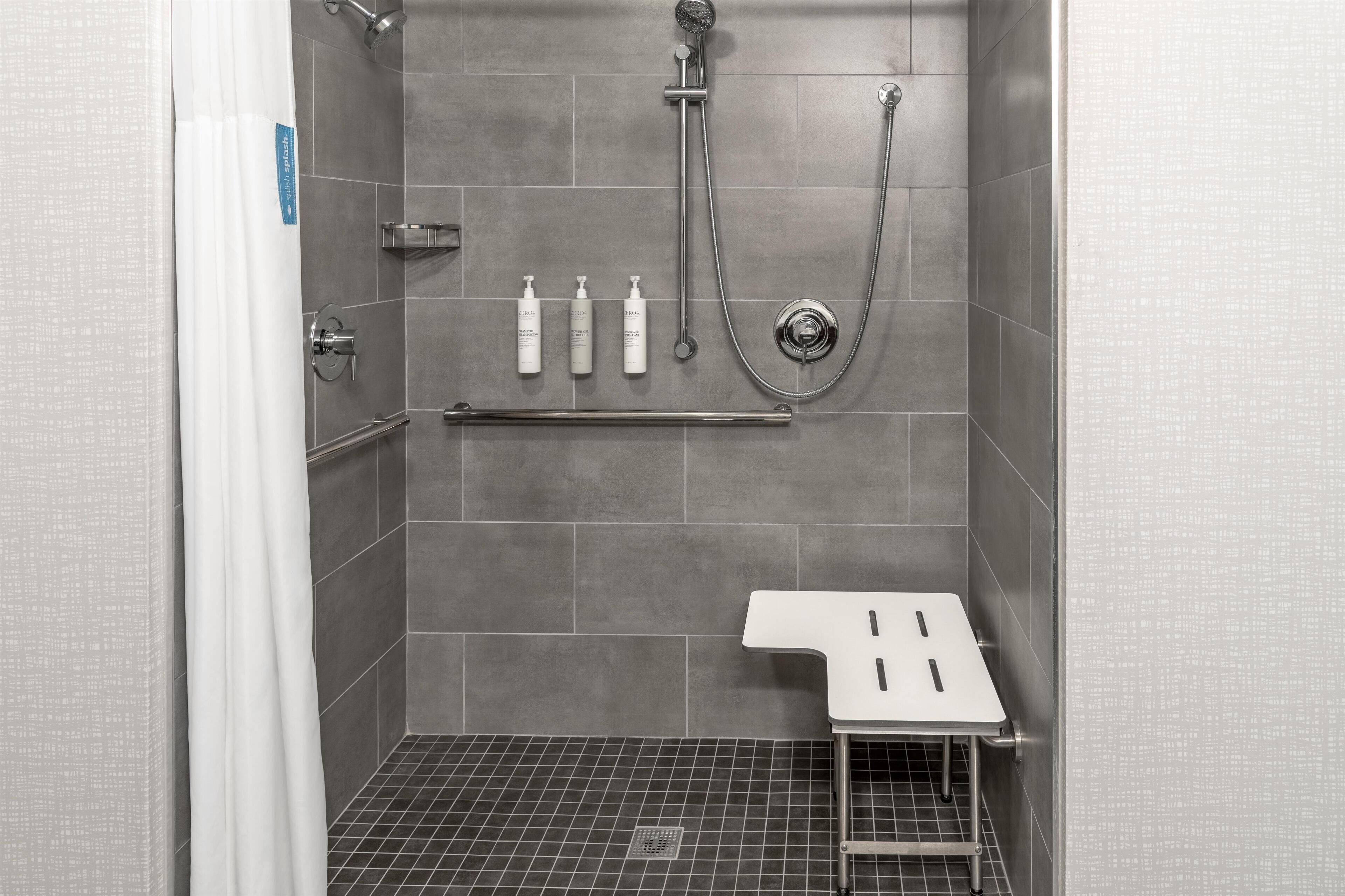 A shower area with a tiled floor, a handheld showerhead, a wall-mounted faucet, and a shelf with toiletries.