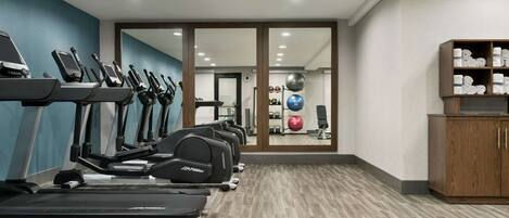 A gym with treadmills, exercise balls, and a wooden cabinet with towels.