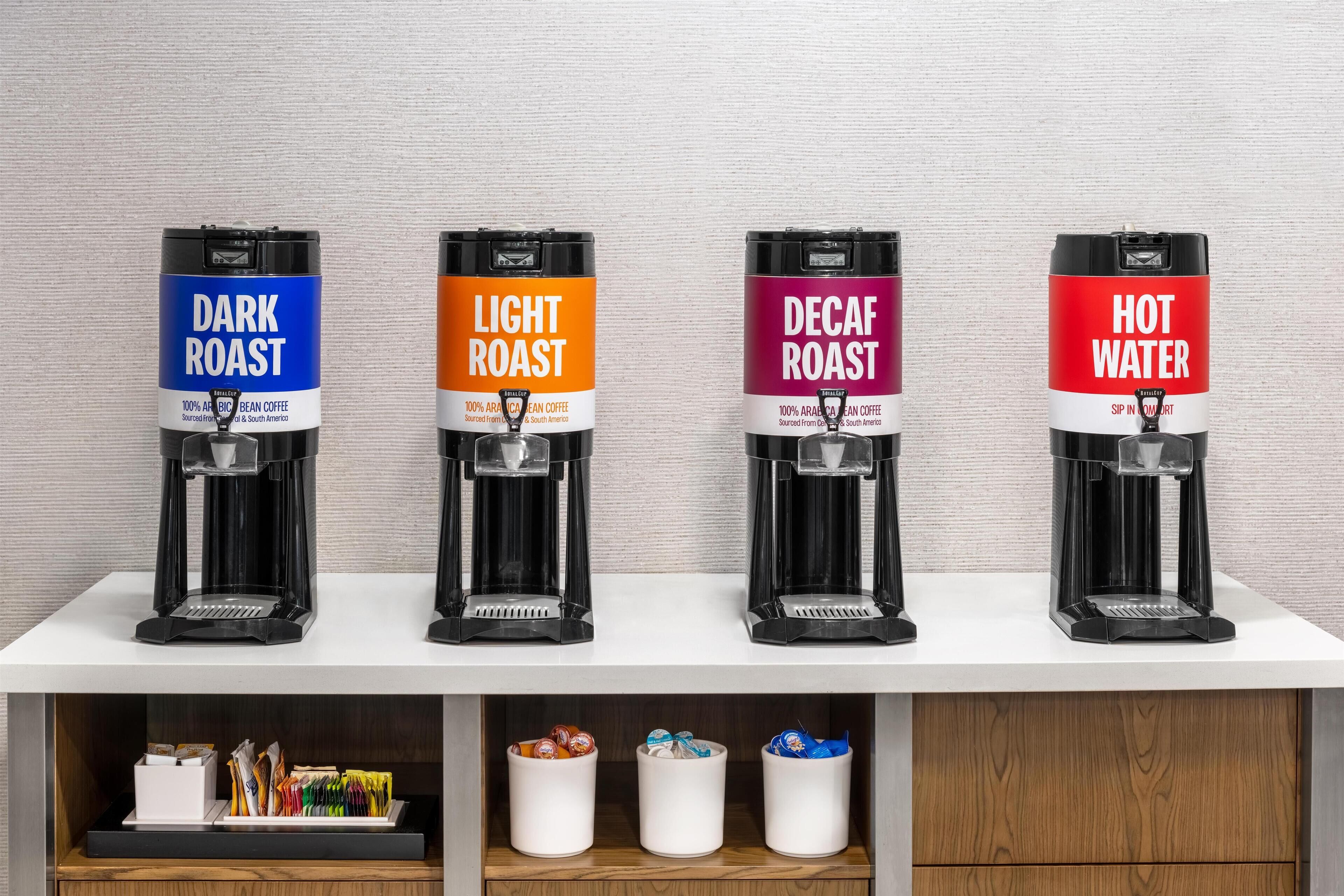 Four coffee machines labeled Dark Roast, Light Roast, Decaf Roast, and Hot Water on a white shelf.