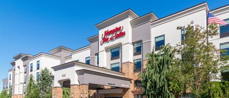 A Hampton Inn & Suites hotel with a modern facade, a welcoming entrance, and an American flag.