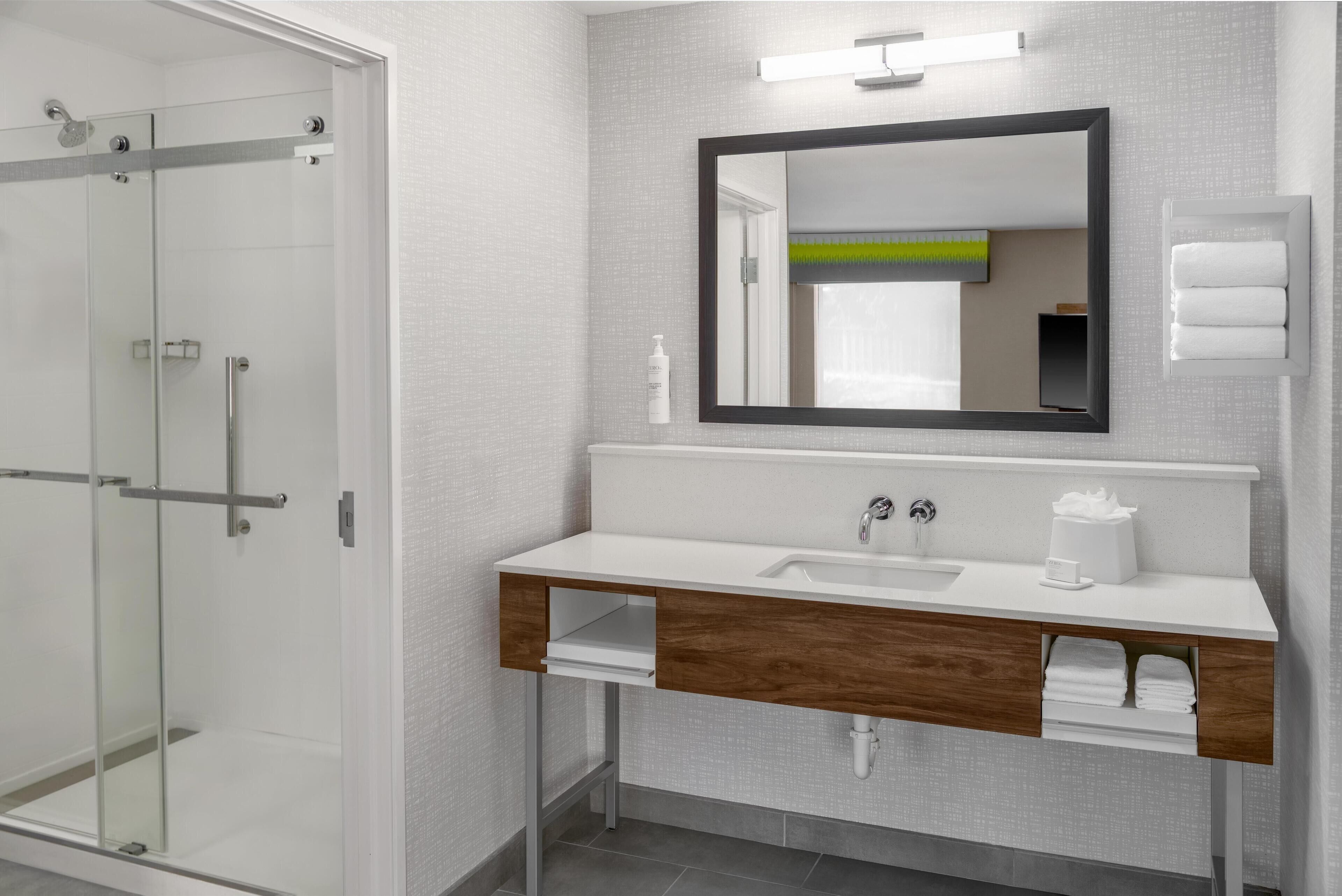 A modern bathroom with a glass shower enclosure, a white sink with a wooden vanity, and a large mirror above the sink.