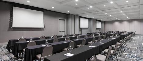 Una sala de conferencias con filas de mesas, sillas y una gran pantalla.