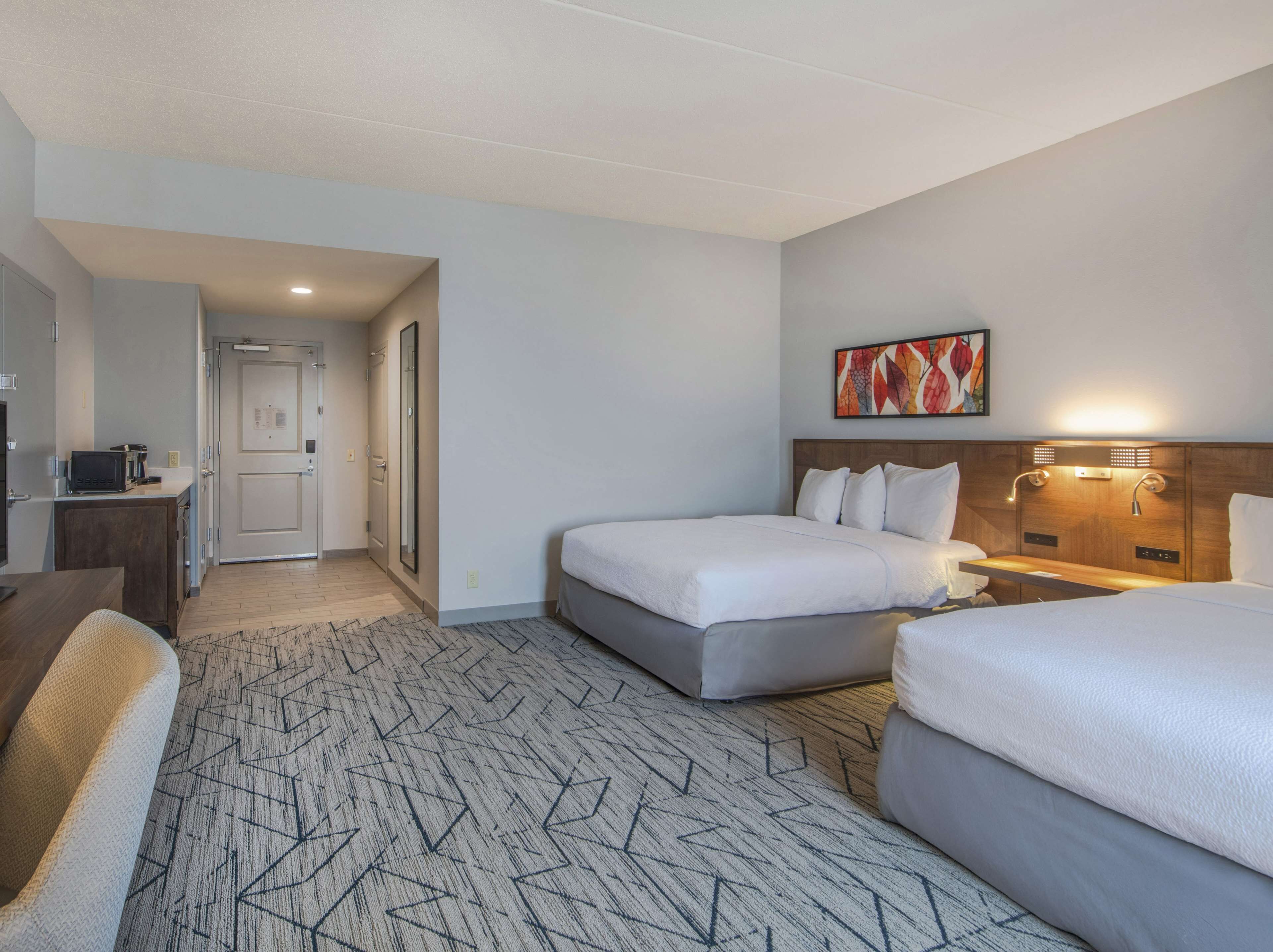 A hotel room with a bed, a desk, a chair, a painting, and a shower area.