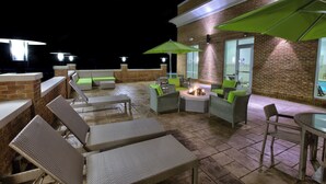 Eine Dachterrasse mit Korbmöbeln, grünen Sonnenschirmen und einer Feuerstelle.