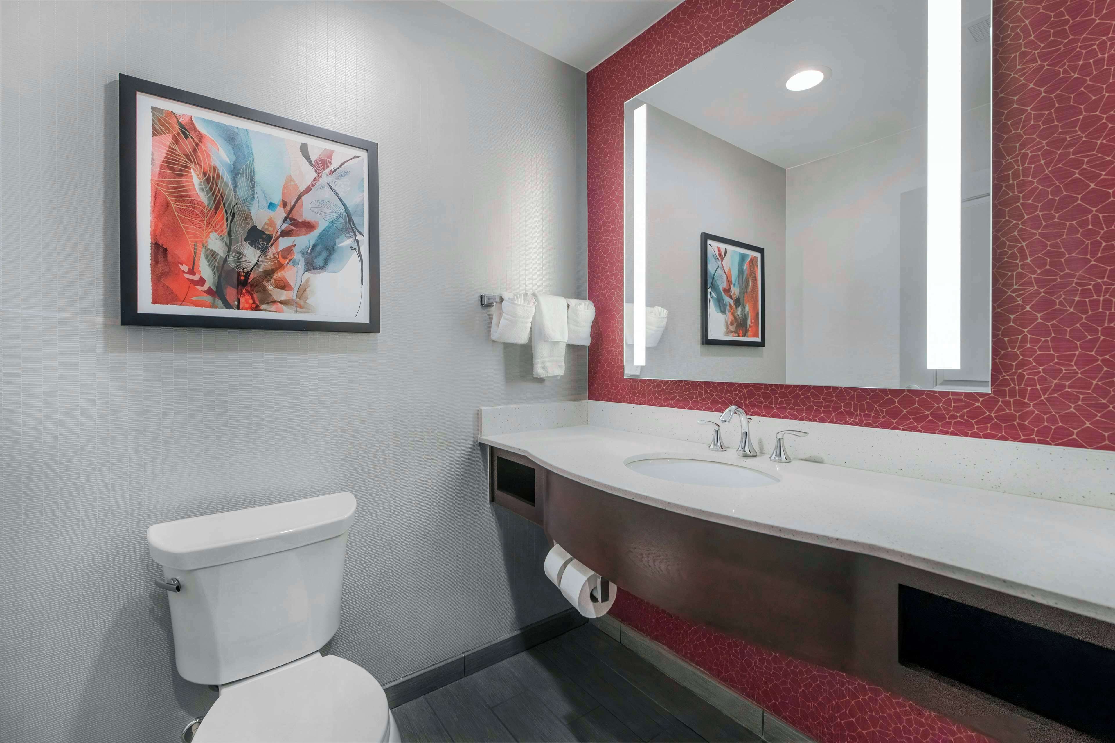 A modern bathroom with a white toilet, a large sink, and a mirror with a red accent wall.