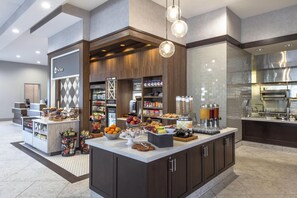 A modern hotel lobby with a self-service breakfast area, a reception desk, and a visible 'The Shop' sign.