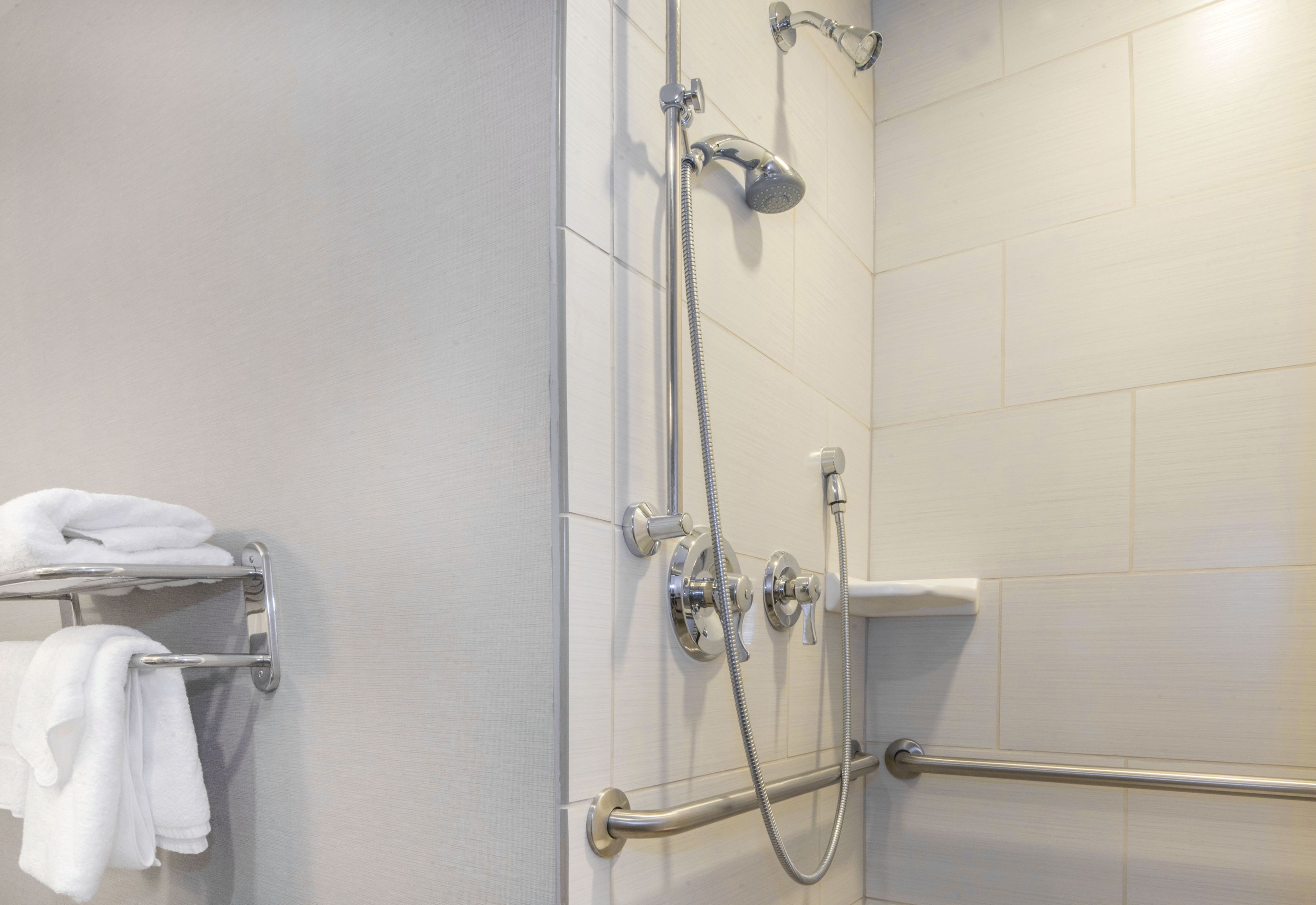 A shower area with a grab bar, a towel rack with towels, and a showerhead.