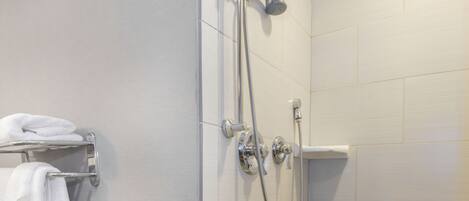A shower area with a grab bar, a towel rack with towels, and a showerhead.