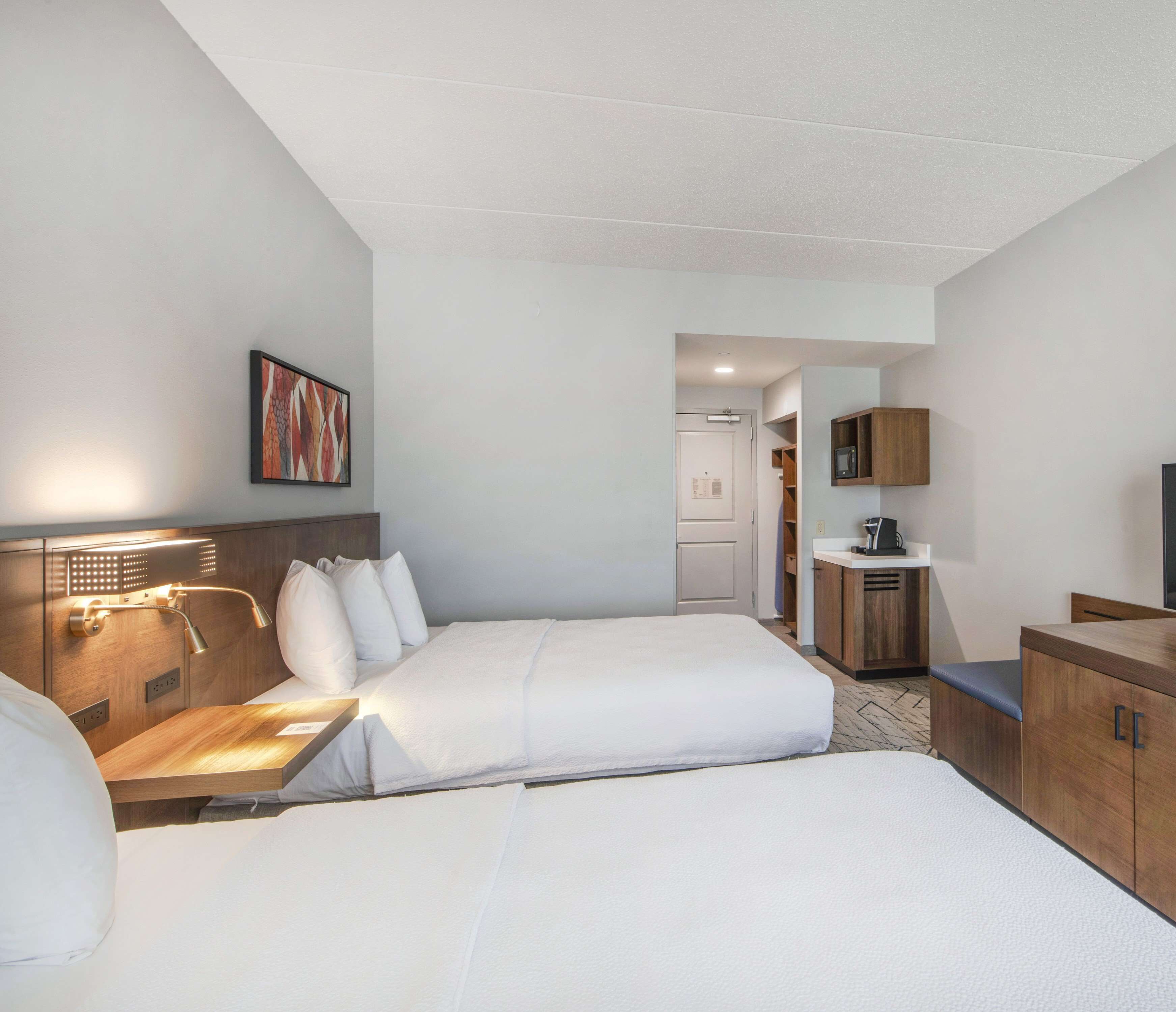 Habitación de hotel con dos camas, un escritorio, una silla, un televisor y una kitchenette pequeña.