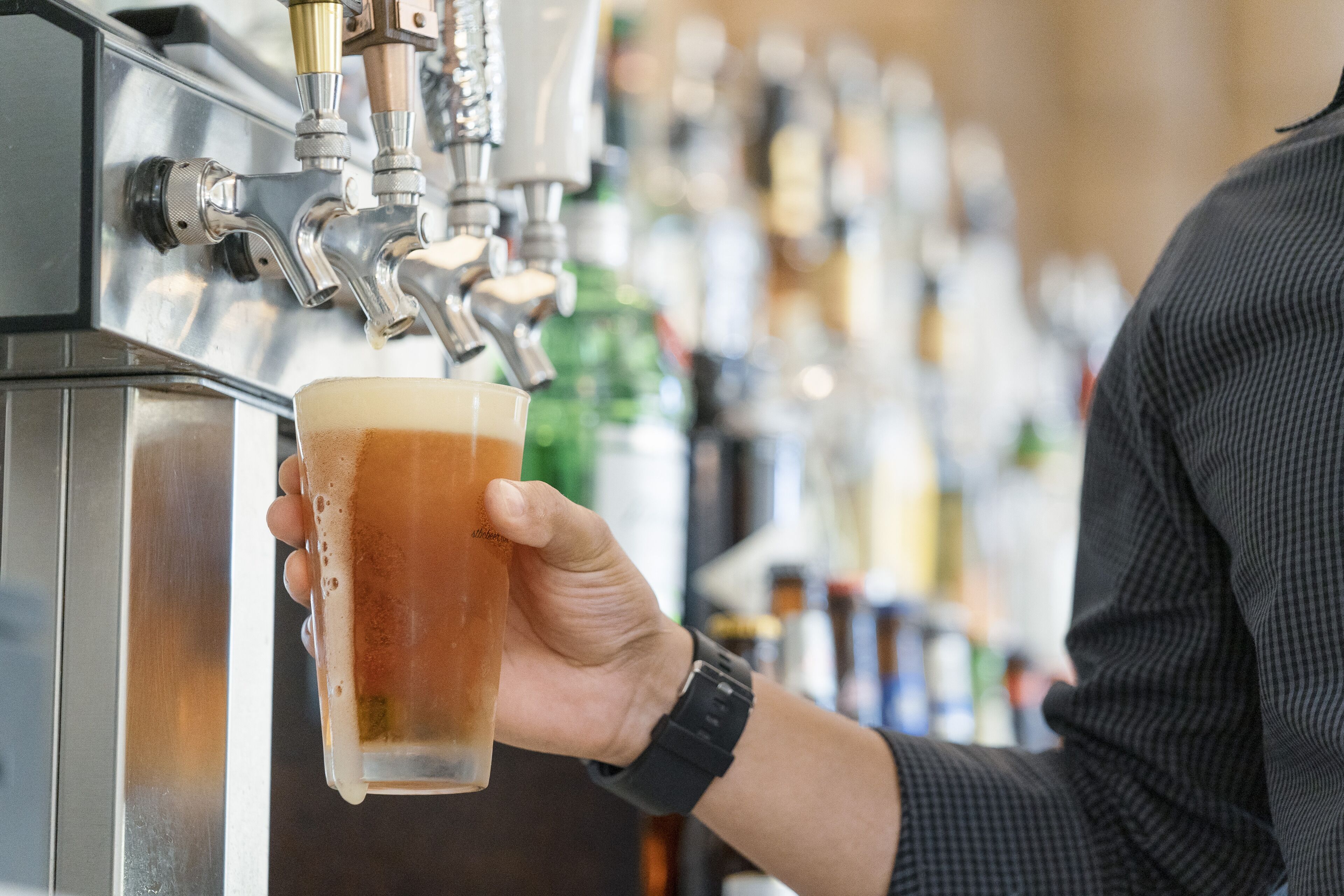 Eine Hand hält ein Glas Bier vor einem Zapfhahn.