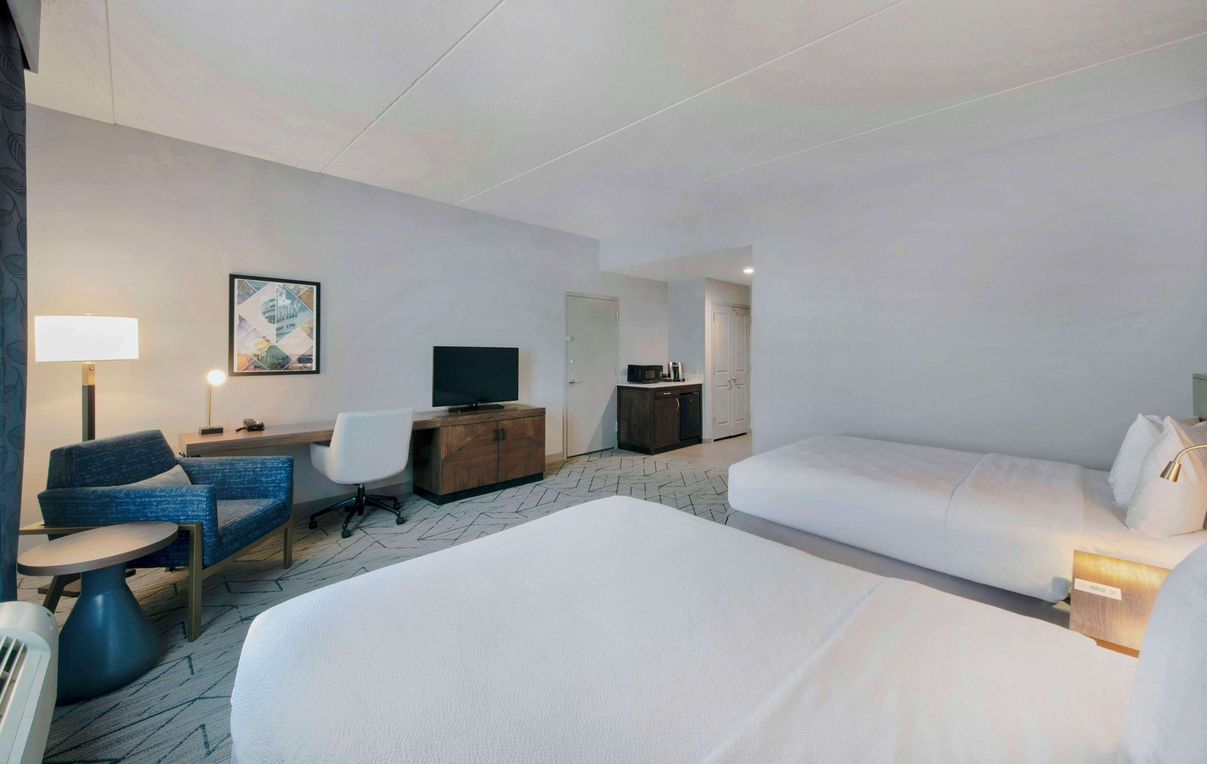 A hotel room with a large bed, a desk with a computer, a chair, a TV, and a small table.