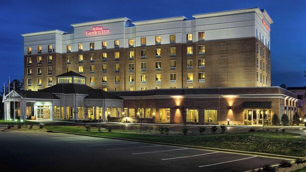 A multi-story hotel with a prominent 'Hilton Garden Inn' sign, a parking lot, and a well-lit entrance.