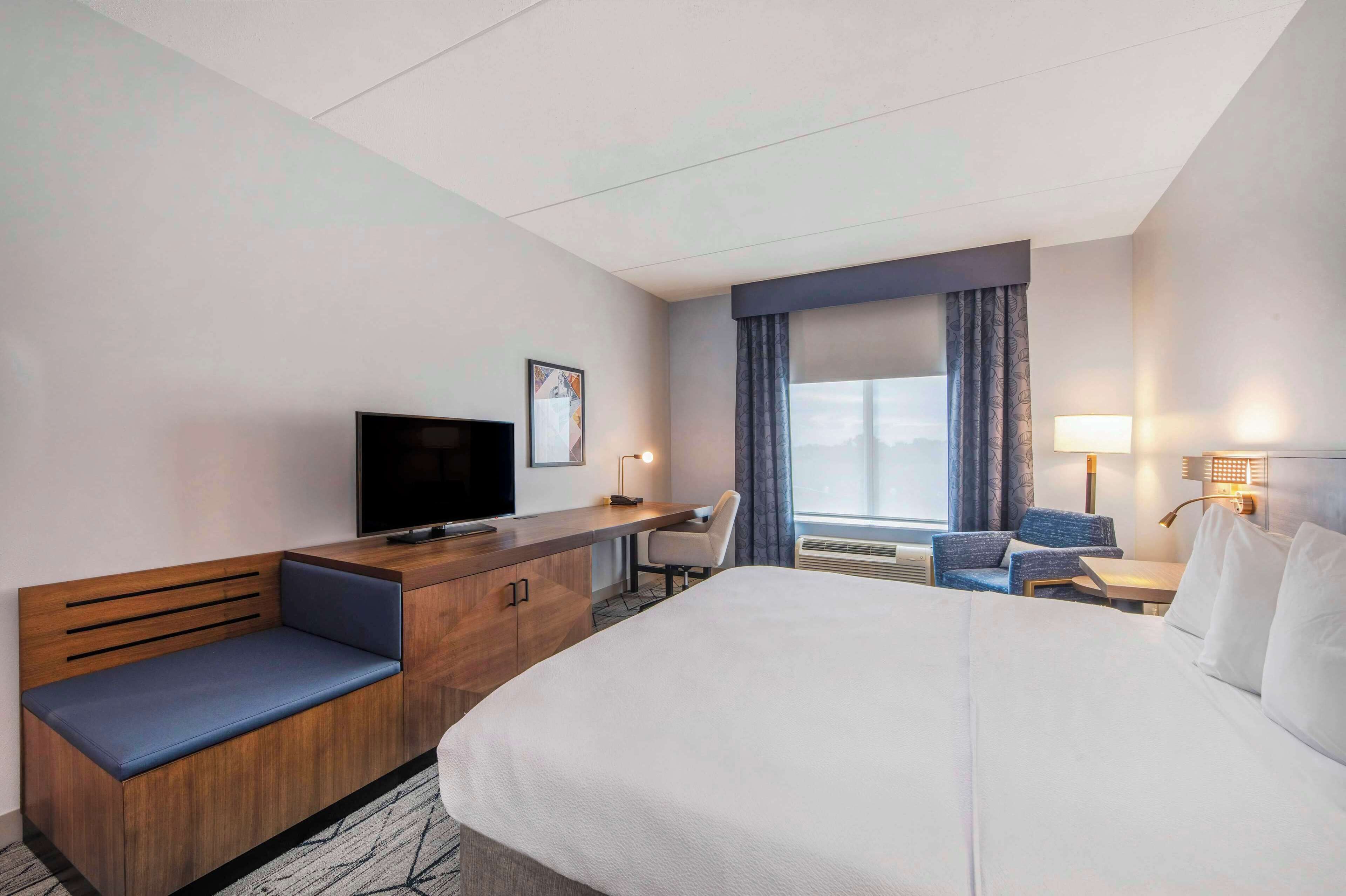 Habitación de hotel con una cama grande, un escritorio de madera con una silla, un televisor y una ventana con cortinas.