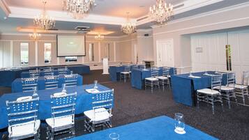 Un salón de conferencias con varias mesas y sillas, una pantalla de proyector y candelabros.