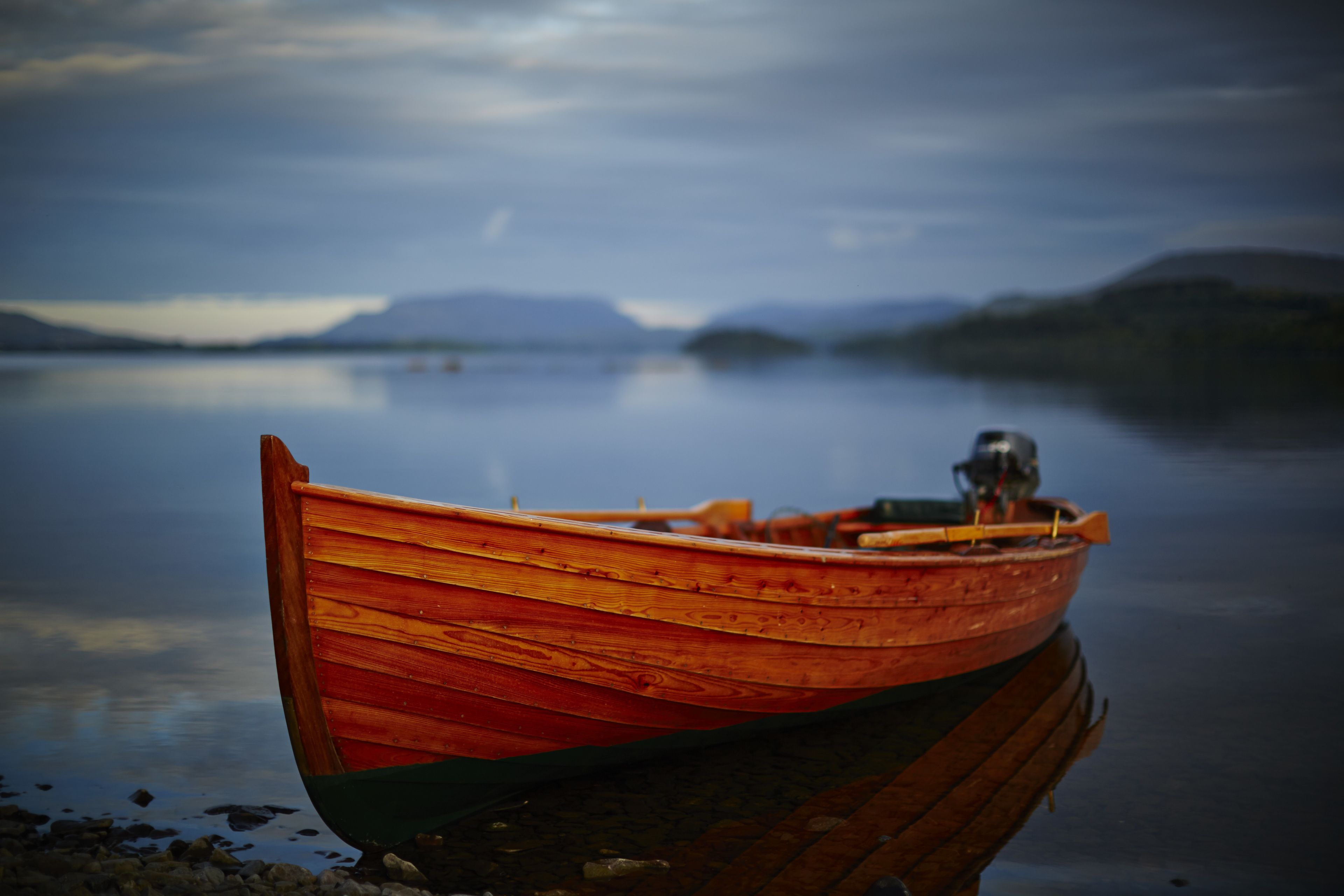 A wooden boat on calm water with a distant mountain range.