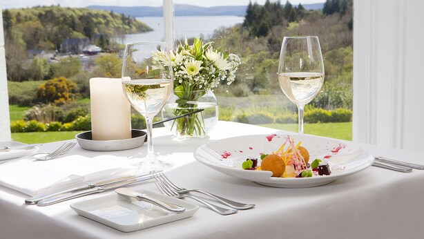 Una mesa dispuesta con vajilla blanca, una vela y un florero, con vistas a un paisaje de un lago y vegetación.