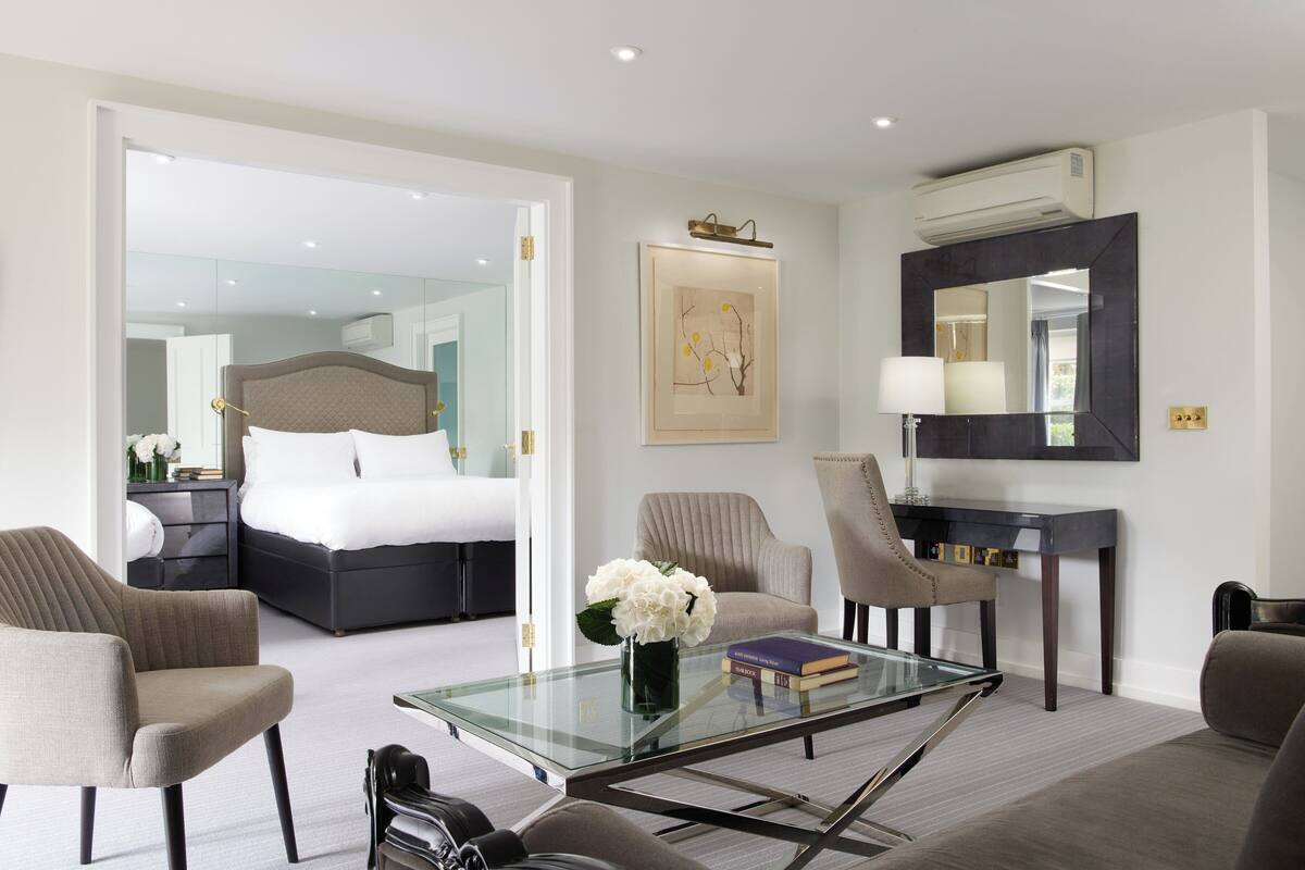 A modern hotel room with a large bed, a glass coffee table, and a seating area with chairs.