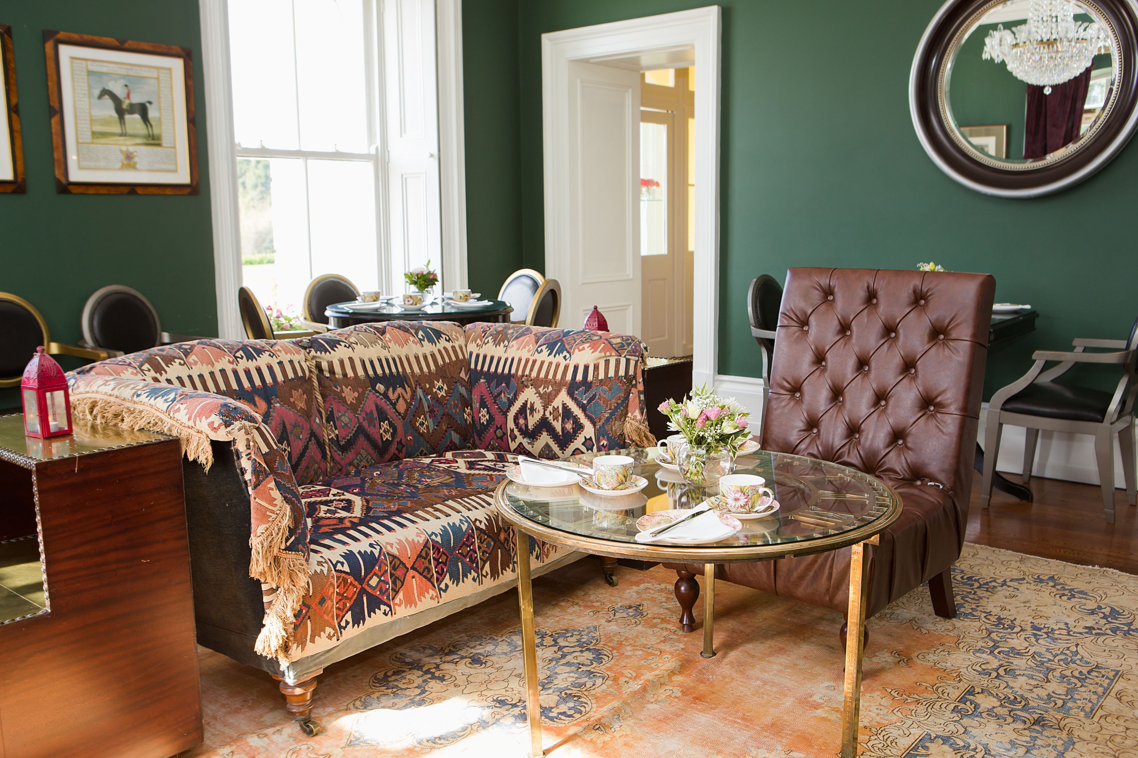 A room with a patterned sofa, a tufted armchair, a glass coffee table, and a mirror on the wall.