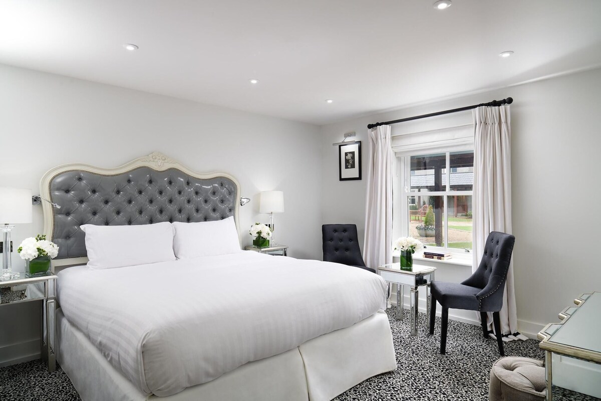Ein Hotelzimmer mit einem großen Bett, einem Sessel, einem kleinen Tisch und einem Fenster mit Vorhängen.