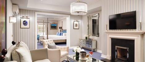 A hotel room with a large bed, a sitting area with a coffee table, a television, and a fireplace.