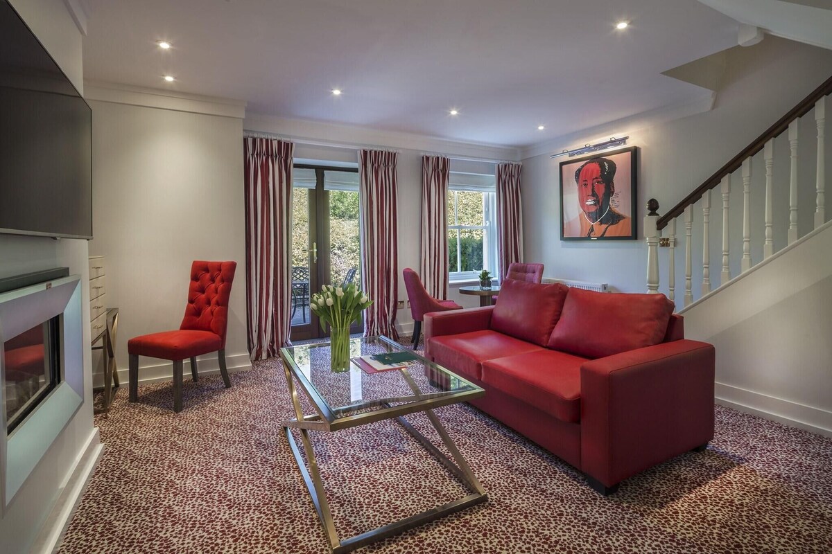 Ein Wohnzimmer mit einem roten Sofa, einem Glastisch, einem roten Sessel, einem Kamin und einer Treppe.