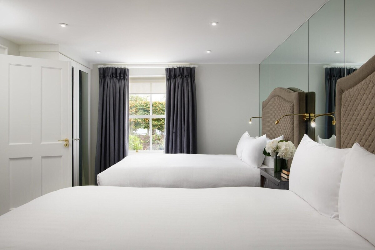 Ein Hotelzimmer mit zwei Betten, einem großen Spiegel und einem Fenster mit Vorhängen.