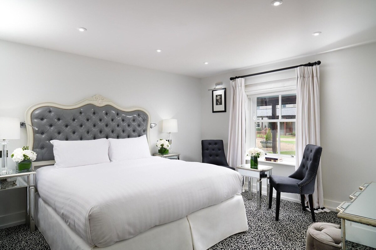 Ein Hotelzimmer mit einem großen Bett, einem Sessel, einem kleinen Tisch und einem Fenster mit Vorhängen.