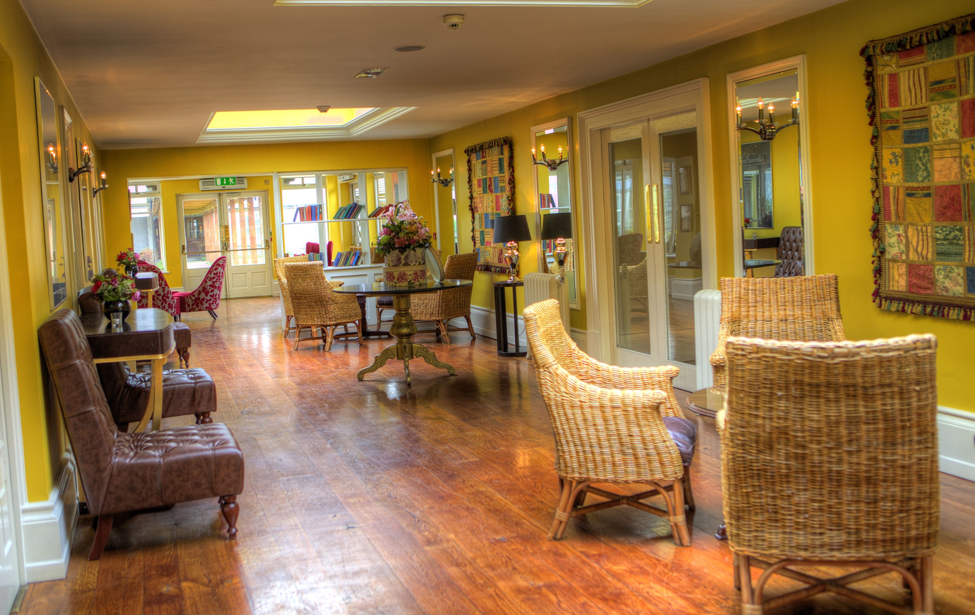 A spacious room with wooden flooring, wicker furniture, and a large window providing natural light.