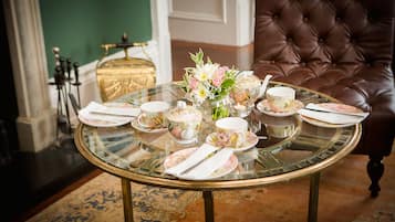 A dining table set with floral tableware and a vase of flowers, surrounded by a brown leather armchair and a gold decorative box.