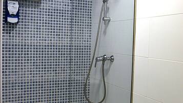 Ducha con paredes de vidrio y revestimiento de azulejos, inodoro blanco y toallero.
