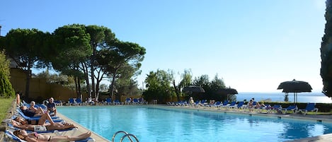 Una piscina al aire libre, sombrillas, sillones reclinables de piscina