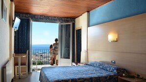 Habitación de hotel con cama, escritorio, silla y balcón con vista al mar.