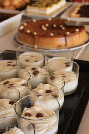 A tray of desserts including a cake and parfaits in glasses. - Hotel Grecs (Roses)