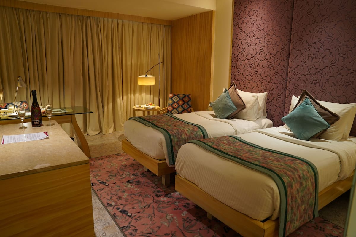 Een hotelkamer met twee bedden, een bureau met lamp, een stoel en een tafel met fles en glazen.