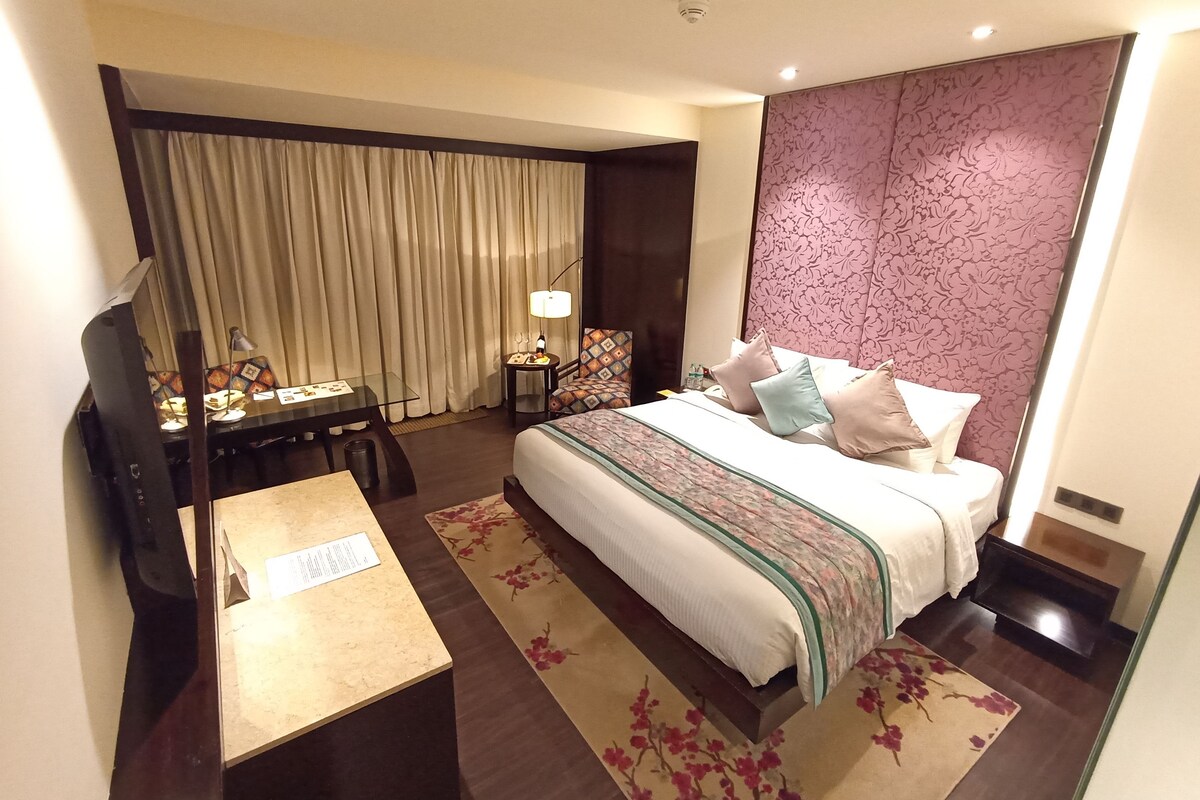 Une chambre d’hôtel avec un grand lit, un bureau, une chaise, une télévision et un rideau.