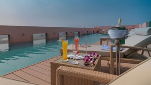 Zona junto a la piscina con sillones, una mesa con bebidas y vistas a la piscina.