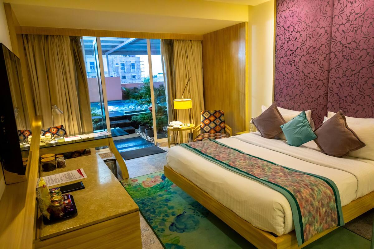 Een hotelkamer met een bed, een bureau met een lamp, een televisie en uitzicht naar buiten.