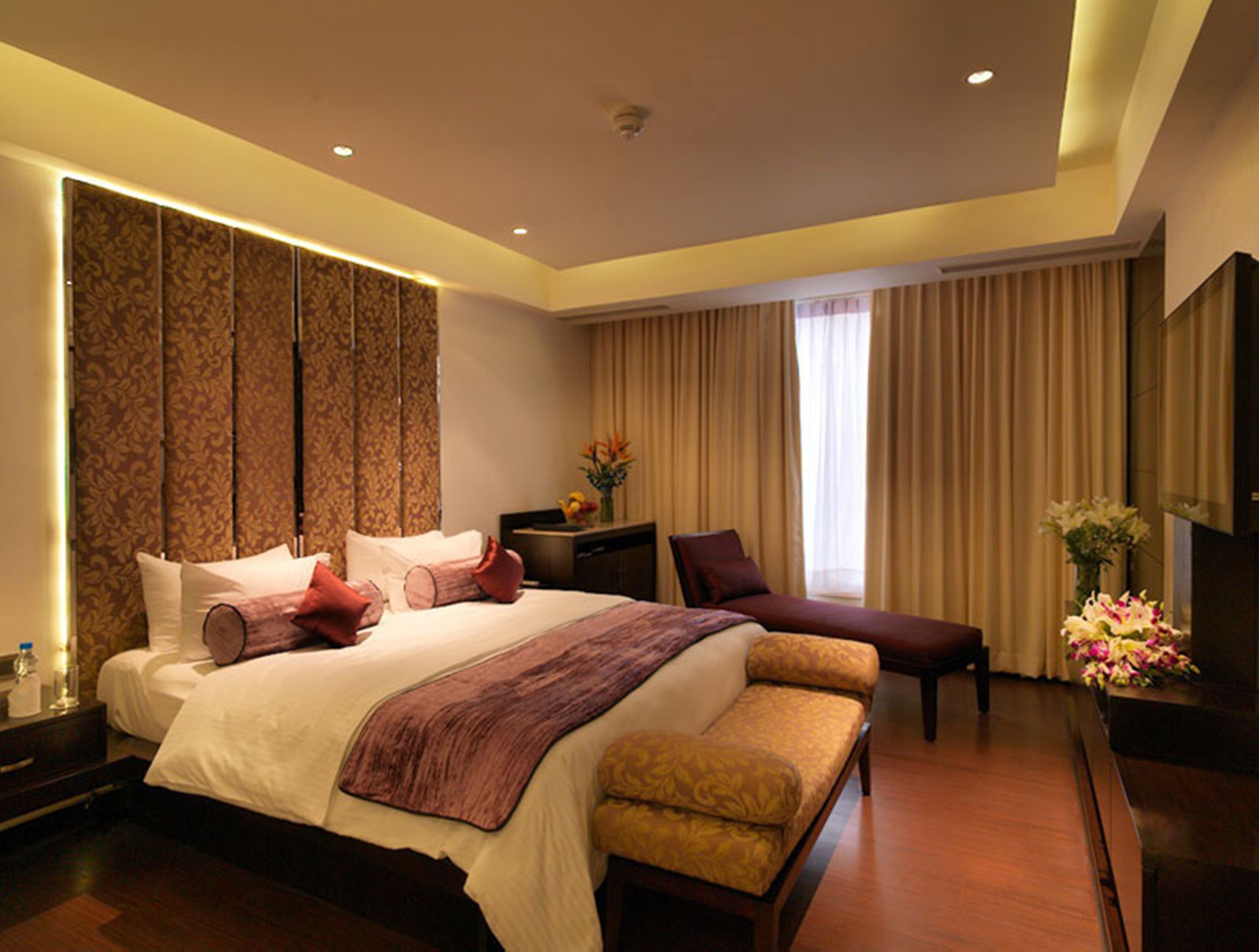 A modern hotel room with a large bed, a desk, a chair, and a bench.