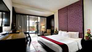 Una habitación de hotel moderna con una cama grande, un escritorio, una silla, un televisor y vistas al exterior.