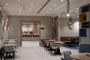 Un interior moderno con una zona de recepción, mesas de comedor, sillas y un elemento decorativo de iluminación.
