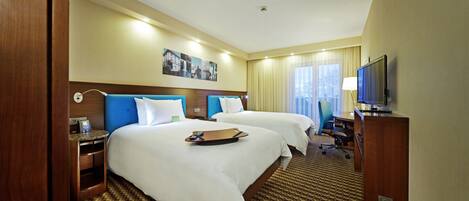 Habitación de hotel con dos camas, un escritorio, televisor y ventana con cortinas.
