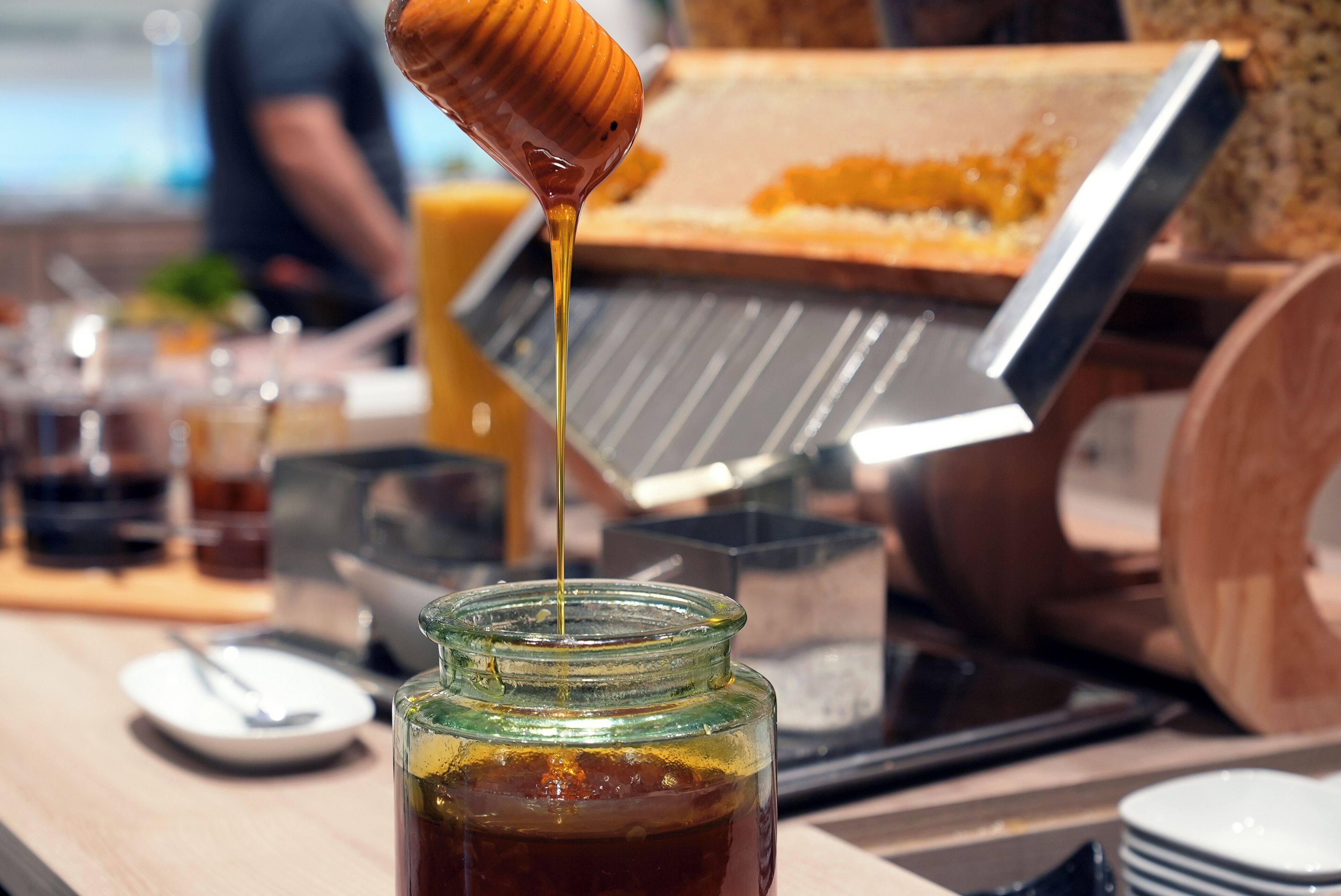A honey jar with honey being poured into a glass.