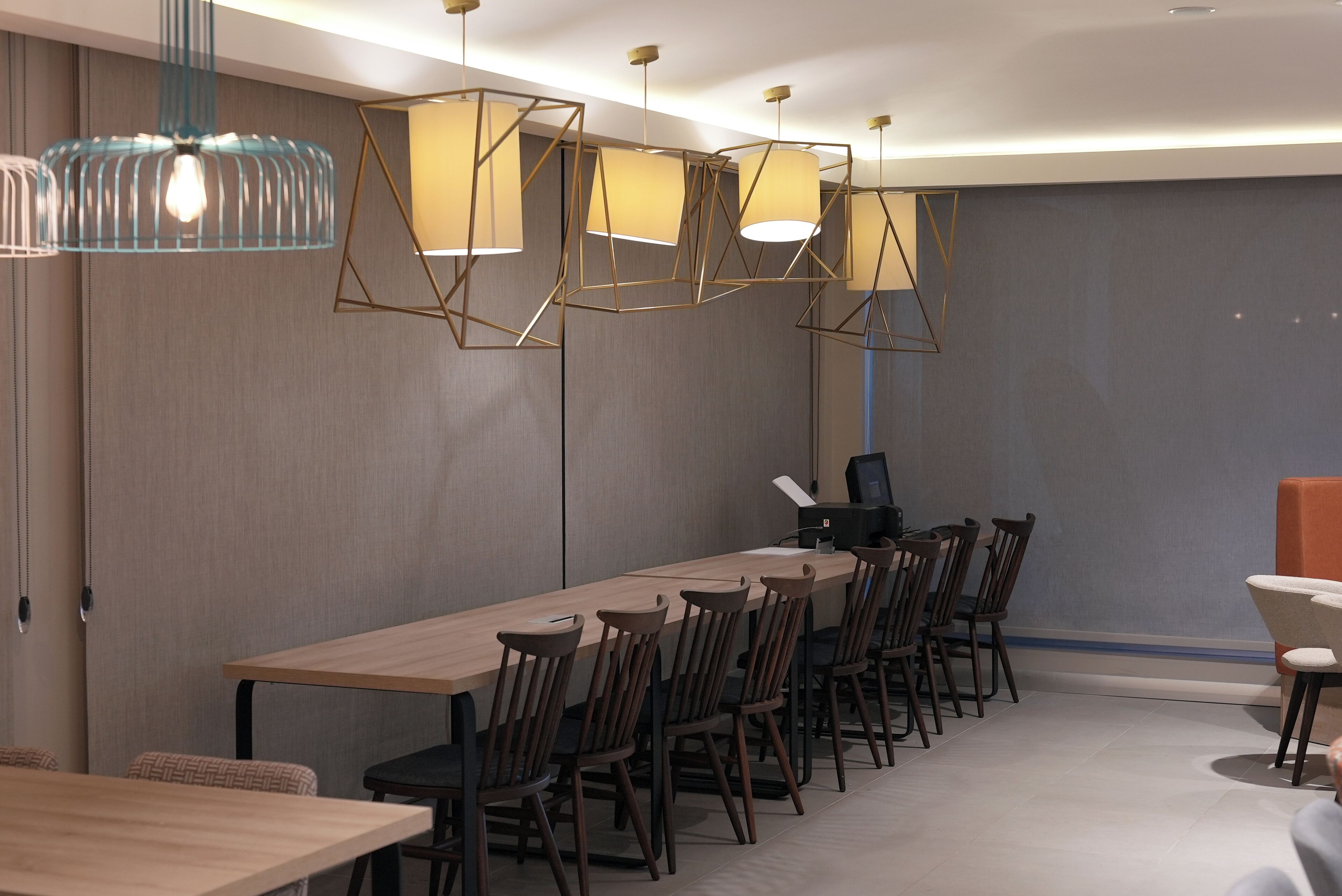 A modern conference room with a long table, multiple chairs, and geometric pendant lighting.