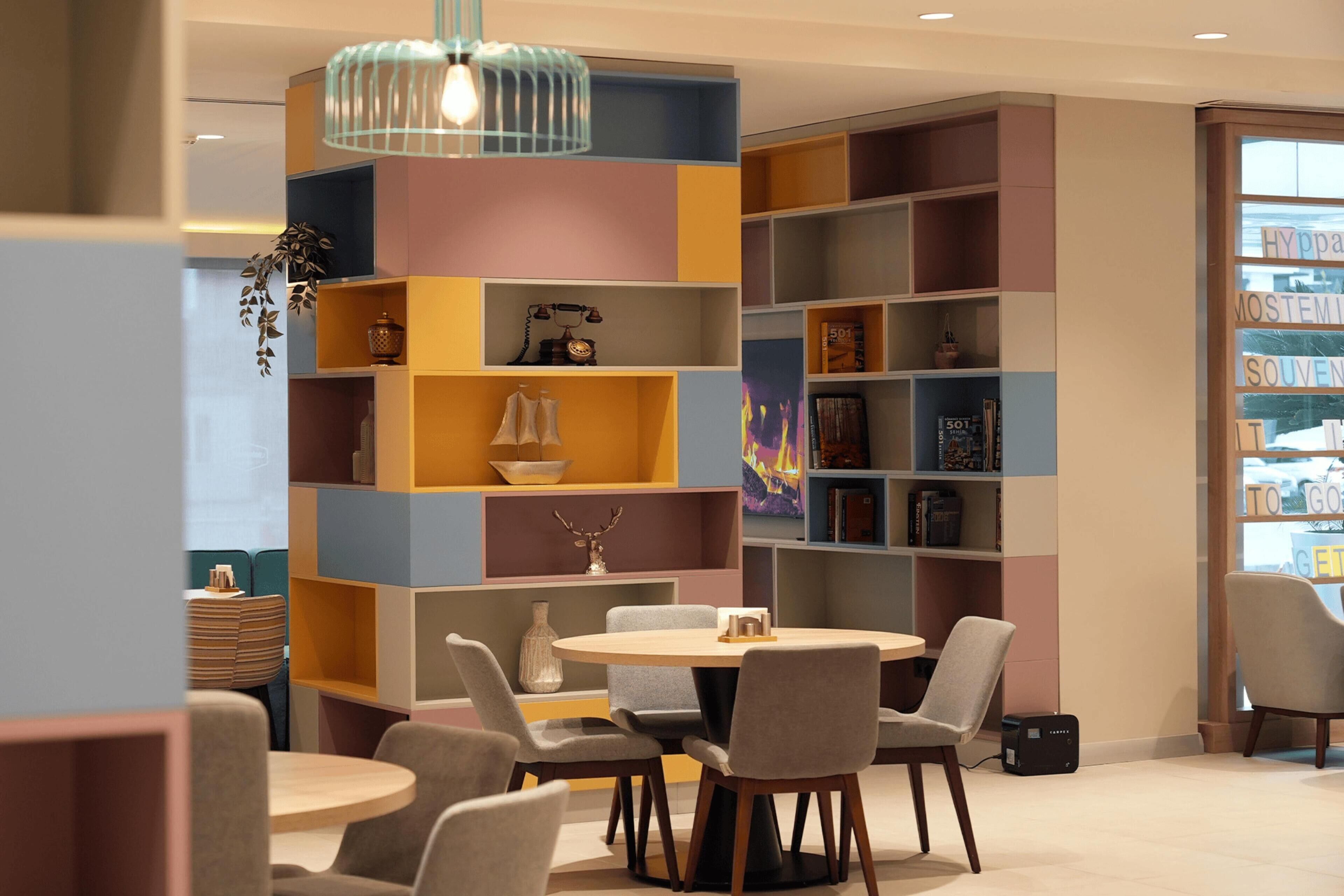 A modern interior with a round table and chairs, a bookshelf with various items, and a hanging light fixture.