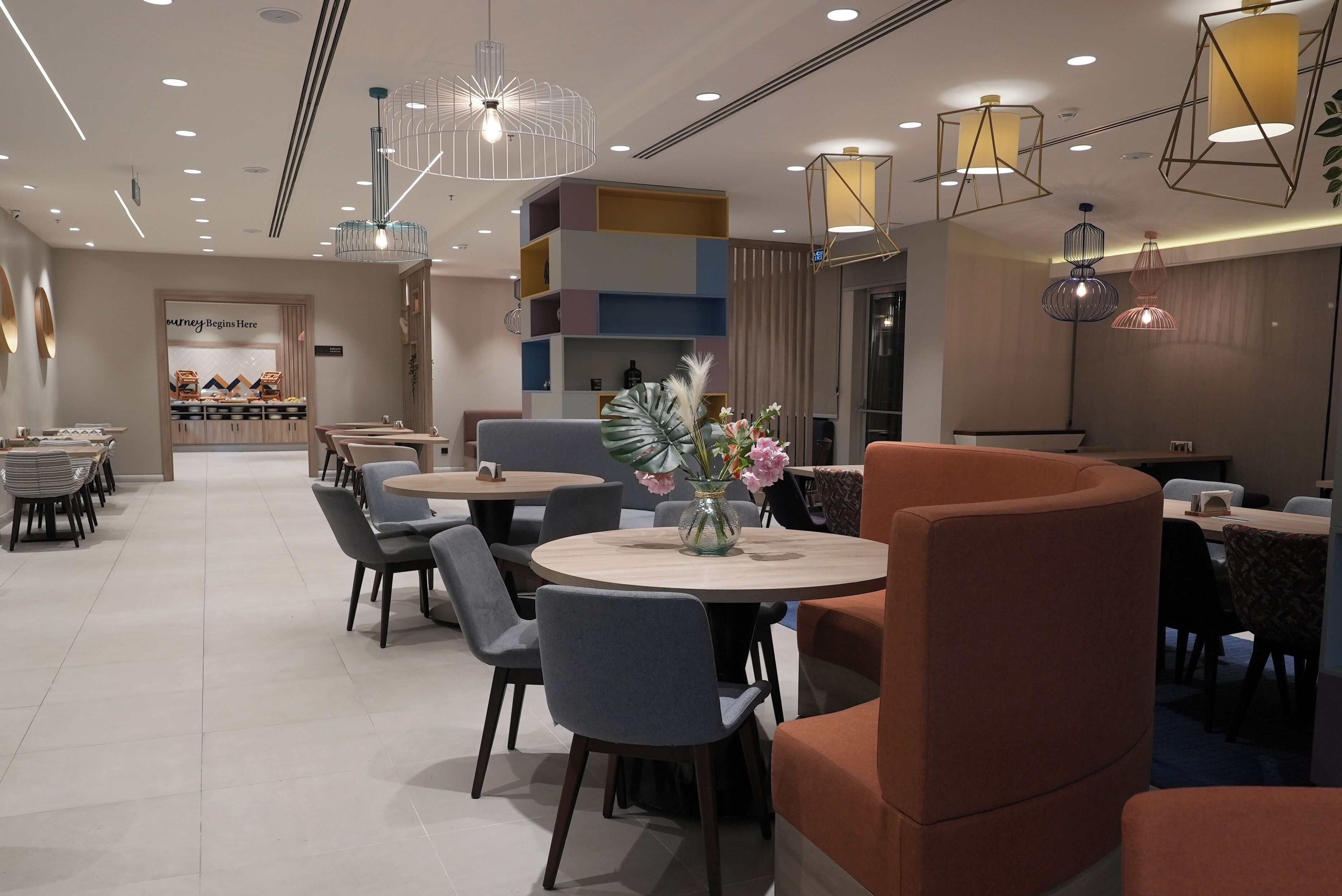 Un comedor moderno con mesas redondas, sillas grises y anaranjadas, y luminarias decorativas.